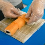 Professional sushi chef preparing roll at commercial kitchen. Cook puts the salmon on roll. Japanese cuisine recipes close-up